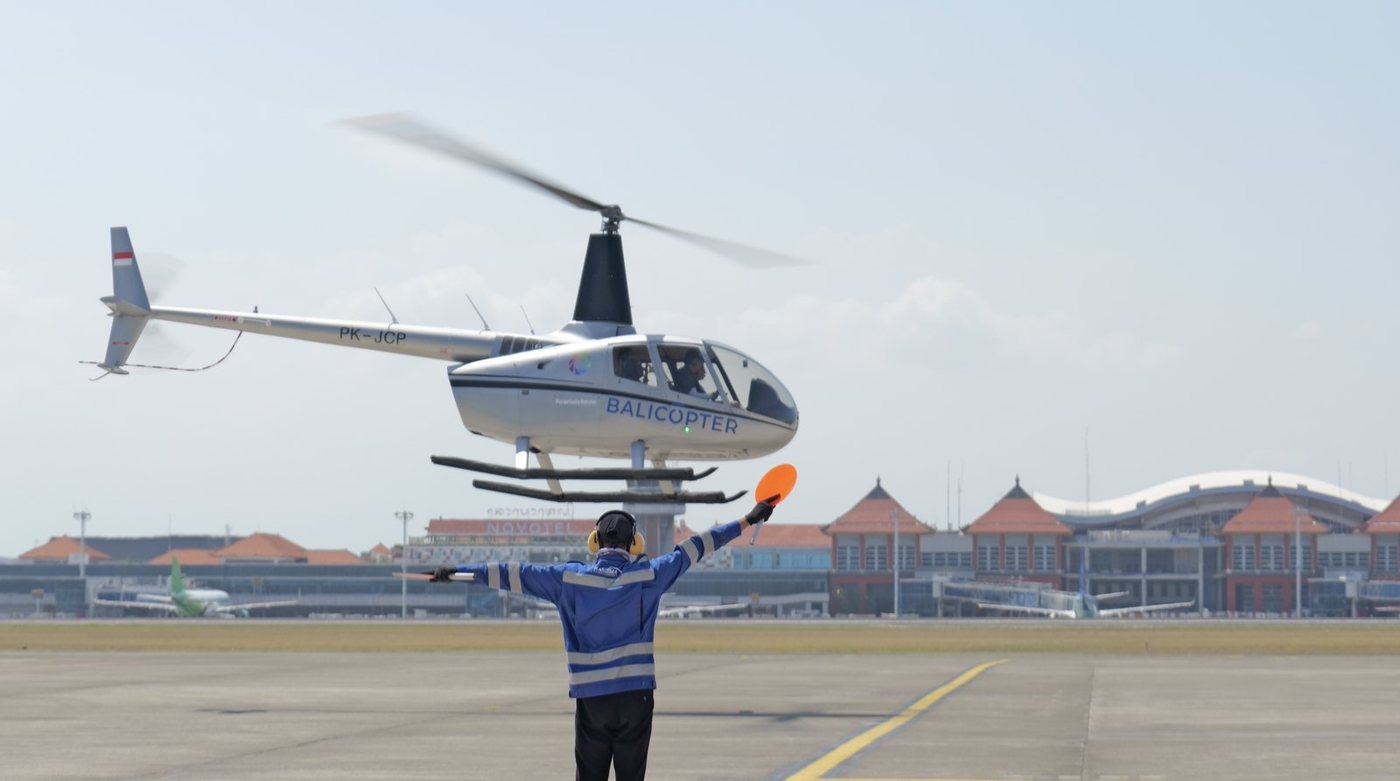 A helicopter on the apron at Ngurah Rai International Airport, guided in by a marshaller